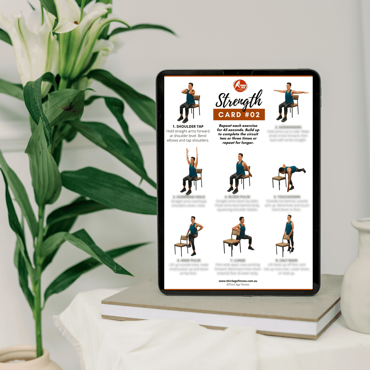 Tablet displaying a strength training card with images of exercises on a white surface with a plant in the background